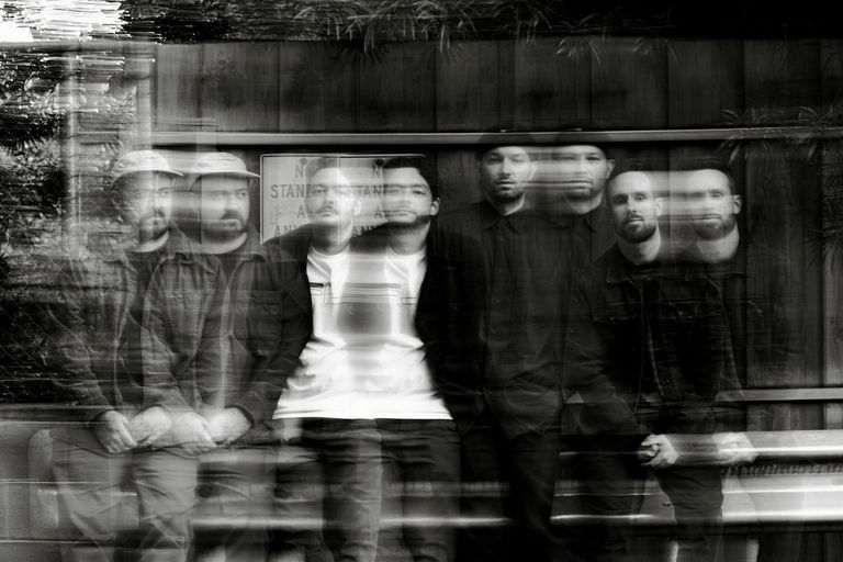 Black and white promo photo of band Heinous Crimes with motion blur effect showing members lined up in front of a wooden fence.